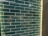 Backlit green subway tile wall behind a bathtub